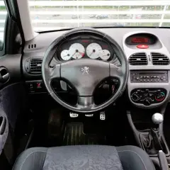 Wnętrze Peugeota 206 1.4 benzyna. Widok na deskę rozdzielczą, kierownicę z logo lwa, radio i dźwignię zmiany biegów.