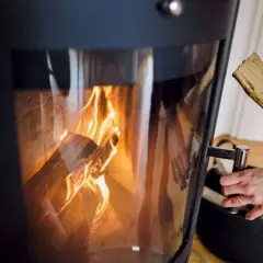 Eine Hand legt Holzscheite nach, um das Feuer im Kamin zu verbrennen. Die Flammen tanzen im Inneren des Ofens.