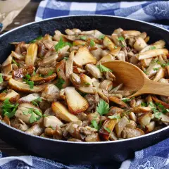 Une poêle débordante de fondue savoyarde aux cèpes, garnie de persil frais. Une cuillère en bois repose sur ce délice forestier.