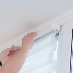 Ręce montują nową tkaninę w rolecie dzień noc, dopasowując ją do mechanizmu.