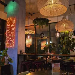 Wnętrze restauracji "Garnizon" z neonem "#POCZUJSIĘ SWOBODNIE", plecionymi lampami i roślinnością.