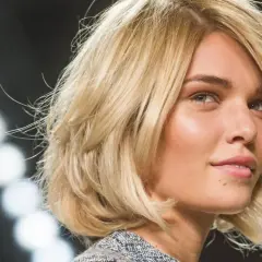 Blonde Frau mit einem stufigen Bob und dicken Haaren, die im Scheinwerferlicht glänzen.