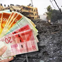 Ręka trzyma banknoty - waluta Izraela, na tle zniszczonego budynku.