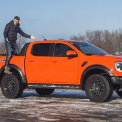 Pomarańczowy Ford Ranger Raptor z kierowcą na pace, gotowy na zimową przygodę nad rzeką.