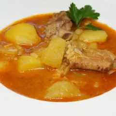 Costillas guisadas con patatas, un plato reconfortante con trozos de carne tierna y patatas en una salsa rojiza, adornado con perejil fresco.