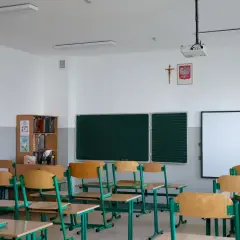 Pusta sala lekcyjna z ławkami, tablicą i projektorem.