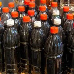 Butelki z ciemnym płynem, być może domowym winem cannonau, stoją obok siebie na półce.