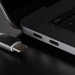 Kabel USB C zbliża się do portu laptopa. Widać jego metalową wtyczkę i biały kabel.