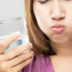 Frau mit geschlossenen Augen hält ein Glas Wasser und spült sich den Mund aus. Ein erfrischendes salzwasser am morgen Ritual.