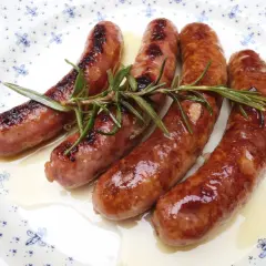 Salchichas doradas en salsa, con romero fresco, servidas en un plato blanco con diseño azul.