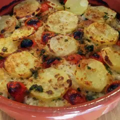 Piatto di riso patate e cozze cotto al forno, con pomodorini e erbe aromatiche, servito in una terrina di terracotta.