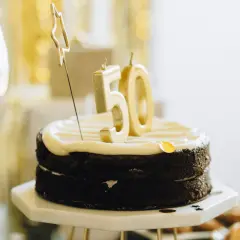 Czekoladowy tort z białym kremem, świeczkami w kształcie cyfry 50 i złotą gwiazdką.