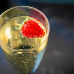 Une fraise flotte dans un verre de soupe angevine pétillante, créant une image rafraîchissante.