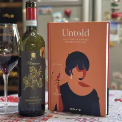 Un bicchiere di vino rosso Nebbiolo d'Alba, una bottiglia e un libro "Untold" sul vino. Le caratteristiche del Nebbiolo sono un viaggio affascinante.