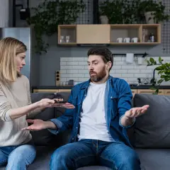 Kobieta z pretensjami pokazuje mężczyźnie telefon, sugerując, że była żona nie spłaca kredytu hipotecznego.