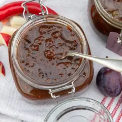 En burk med plommonchutney, perfekt för ett plommon recept. Äpplen, plommon och chili ligger bredvid.