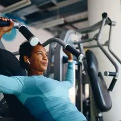 Frau trainiert richtig im Fitnessstudio an einer Brustpresse. Sie konzentriert sich auf die Bewegung und hört Musik über ihre Kopfhörer.