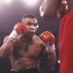 Mike Tyson in his iconic boxing stance, ready to fight. His red gloves are raised, a testament to his legendary career in tysons boxing.