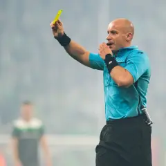 Sędzia piłkarski pokazuje żółtą kartkę, dmuchając w gwizdek.