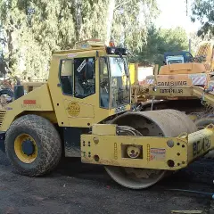 Żółty walec drogowy BOMAG BW 213D-3, obok koparka Samsung Caterpillar. Szerokość koparki nie jest widoczna, ale walec jest imponujący.