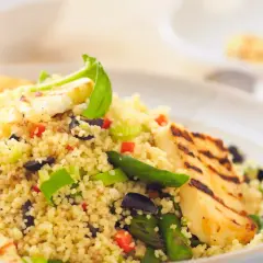 Un piatto colorato di cous cous con verdure miste, olive nere e cubetti di formaggio grigliato.