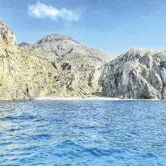 Aguas azules bañan la costa rocosa de una cala en Almería. Montañas escarpadas y una pequeña playa de arena componen el paisaje.