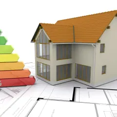 Dom na planach z kolorową drabinką klasyfikacji energetycznej, odzwierciedlającą wymogi ustawy o charakterystyce energetycznej budynków.
