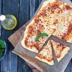 Pyszna margarita pizza z roztopionym serem i bazylią, obok oliwa i świeże liście.