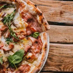 Pyszna pizza carbonara z chrupiącym boczkiem i rukolą, podana na drewnianym stole.