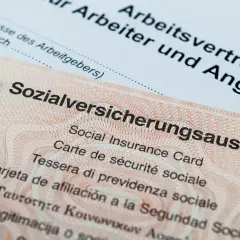 Sozialversicherungsausweis zeigt, wo man die Sozialversicherungsnummer findet. Ein Arbeitsvertrag liegt daneben.