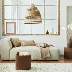 Un salon lumineux avec un canapé beige, des coussins texturés et une couverture. Une idée pour comment agrandir une pièce : misez sur la lumière naturelle et des tons clairs.