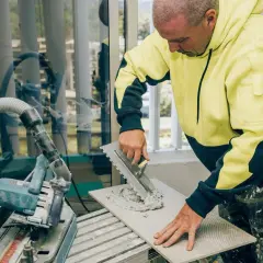 Fachowiec nakłada klej na płytkę 120x60, używając odpowiedniego grzebienia. W tle widać piłę do cięcia płytek.
