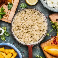 Perfekt gekochtes Quinoa in einer Pfanne, umgeben von frischen Zutaten wie Avocado, Mango und Tomaten.