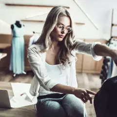 Eine Designerin mit Brille misst Stoff für ihr nächstes Projekt im Bereich IU Modemanagement.