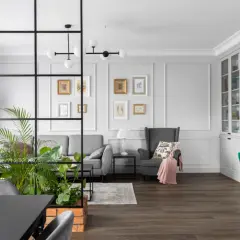 Nowoczesny salon z zieloną ścianą z kwiatów, szarą sofą, fotelem i przeszkloną witryną.