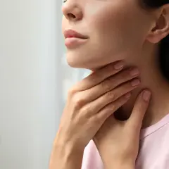 Kobieta dotyka szyi, być może odczuwając dyskomfort związany z tarczycą, który może być leczony np. thyrozolem.
