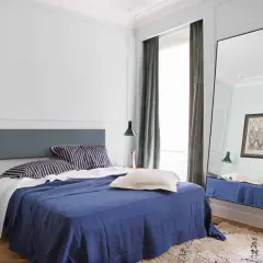 Modern mens bedroom ideas: a navy blue bed with striped pillows, a grey headboard, and a large floor mirror reflecting the room.