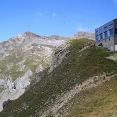 Moderne Hütte am Hang, Teil der Tour des Muverans, mit steilen Felswänden und grünen Bergwiesen im Hintergrund.