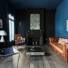 Ein **dunkles Wohnzimmer** mit blau-schwarzen Wänden, Ledersofa, Kamin und moderner Kunst.