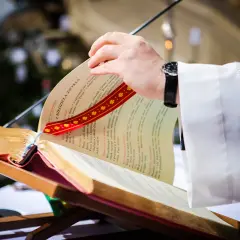 Dłoń księdza przewracająca kartki księgi liturgicznej na pulpicie.