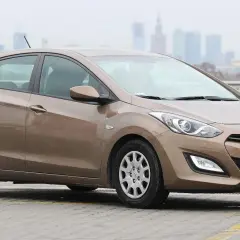 Brązowy Hyundai i30, jedna z popularnych generacji tego modelu, zaparkowany na tle miejskiej panoramy.