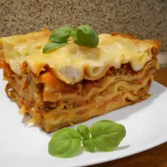 Pyszna, wielowarstwowa lasagne z sosem pomidorowym i serem, ozdobiona listkami bazylii. Idealna inspiracja, jak zrobić lasagne.
