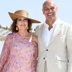 Ana Rosa Quintana y su marido celebran la boda de su hijo. Ella luce un vestido floral y sombrero, él un traje claro.