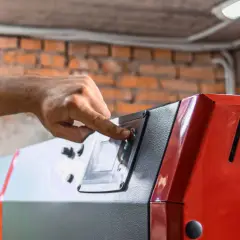 Dłoń reguluje ustawienia pieca na ekogroszek, przygotowując go do trybu zimowego.