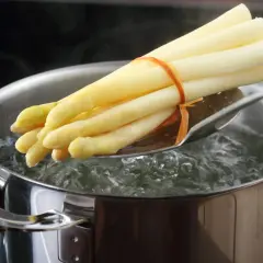 Un bouquet d'asperges blanches est plongé dans l'eau bouillante pour une cuisson parfaite.
