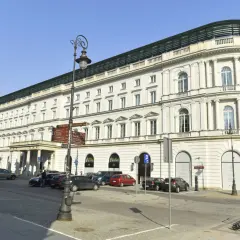 Elegancki, biały budynek hotelowy z kolumnami i łukowymi oknami, przed którym zaparkowane są samochody.