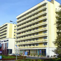 Hotel Vestina w Międzyzdrojach, wysoki, żółty budynek z balkonami, otoczony zielenią.