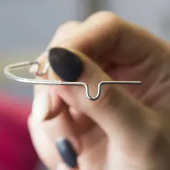 Dłoń trzyma metalowy aparat ortodontyczny, który wygląda jak lip bumper.