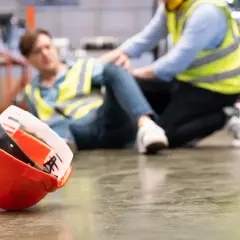 Un lavoratore a terra, un collega preoccupato, un elmetto arancione caduto. Un chiaro segnale di infortunio sul lavoro.