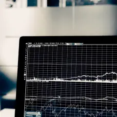 Wykresy na ekranie laptopa pokazują zmienność cen akcji. Analiza tych danych pomaga w ocenie, co to jest scoring finansowy i jak podejmować trafne decyzje inwestycyjne.